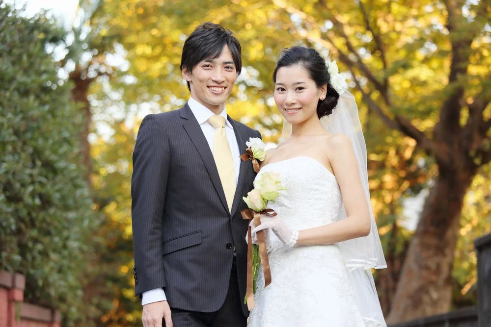 黄葉した木々を背景に、スーツ姿の男性とウェディングドレス姿の女性が微笑んでいる様子
